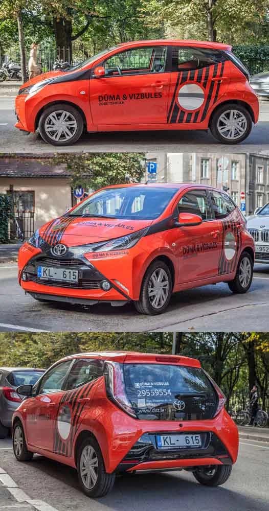 Oranžs un melns Toyota aplīmējums Dūma un Vizbules zīmolam, fotografēts no trim leņķiem pilsētas ielā