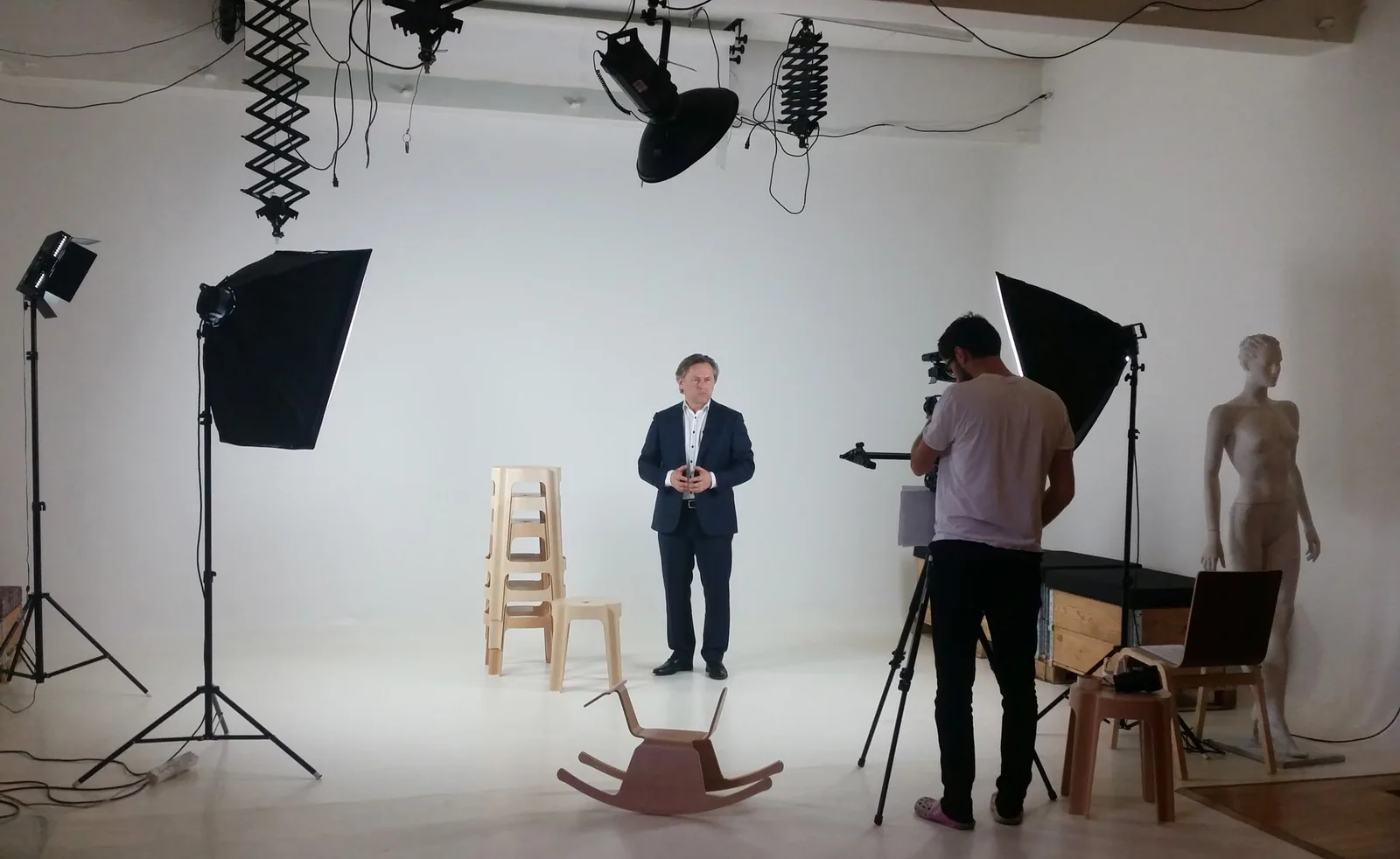 On-camera interview setup with a cameraman filming a presenter beside a mannequin and rocking-horse prop