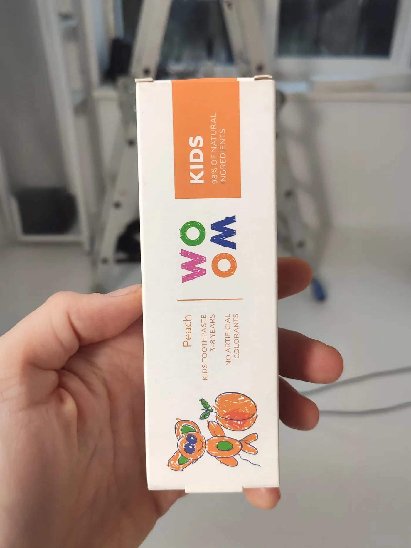 Oriģinālais foto Woom Kids persiku zobu pastas kastītei rokā