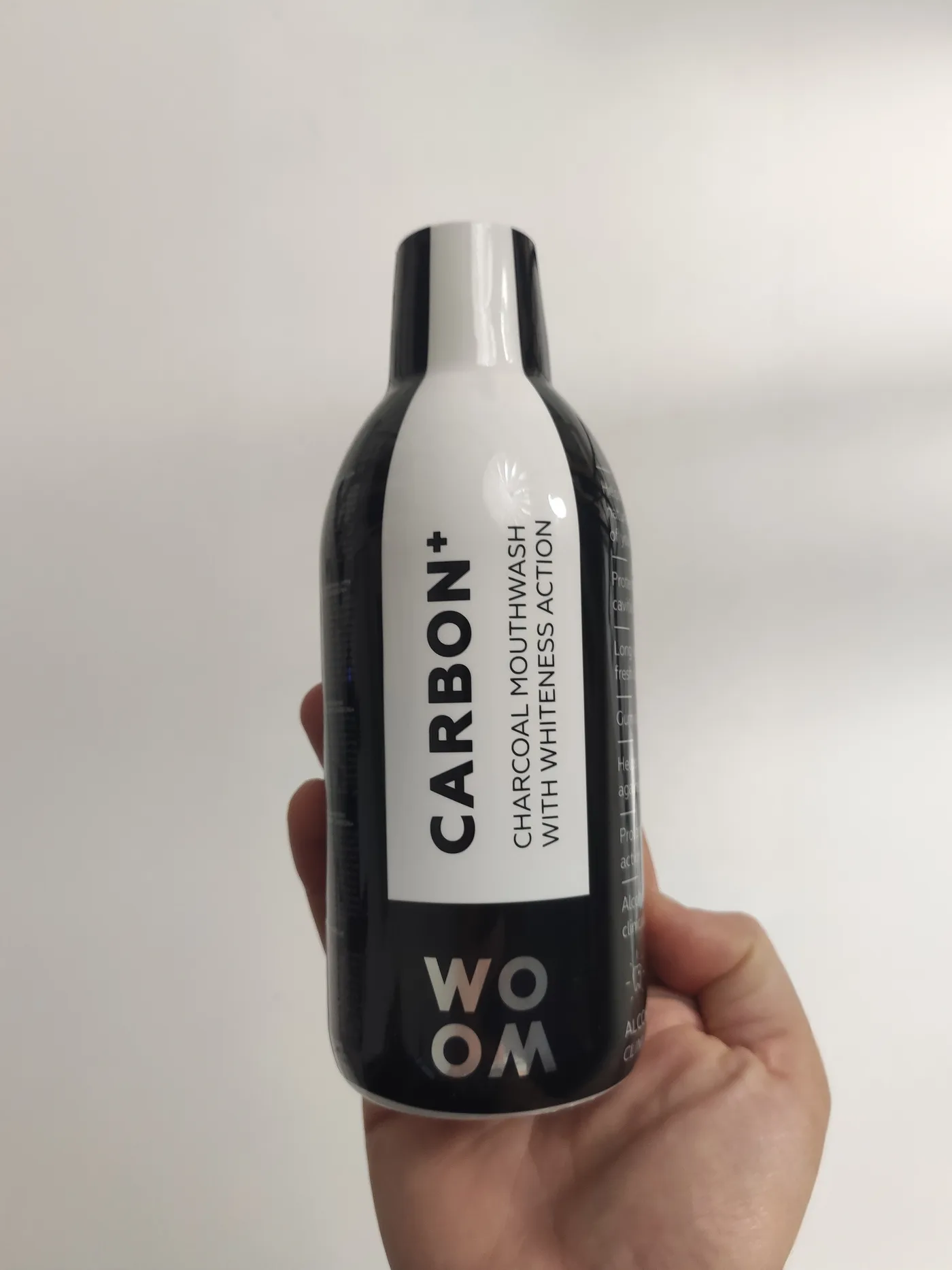 Oriģinālais foto Woom Carbon+ ogles mutes skalojamā līdzekļa pudelei rokā